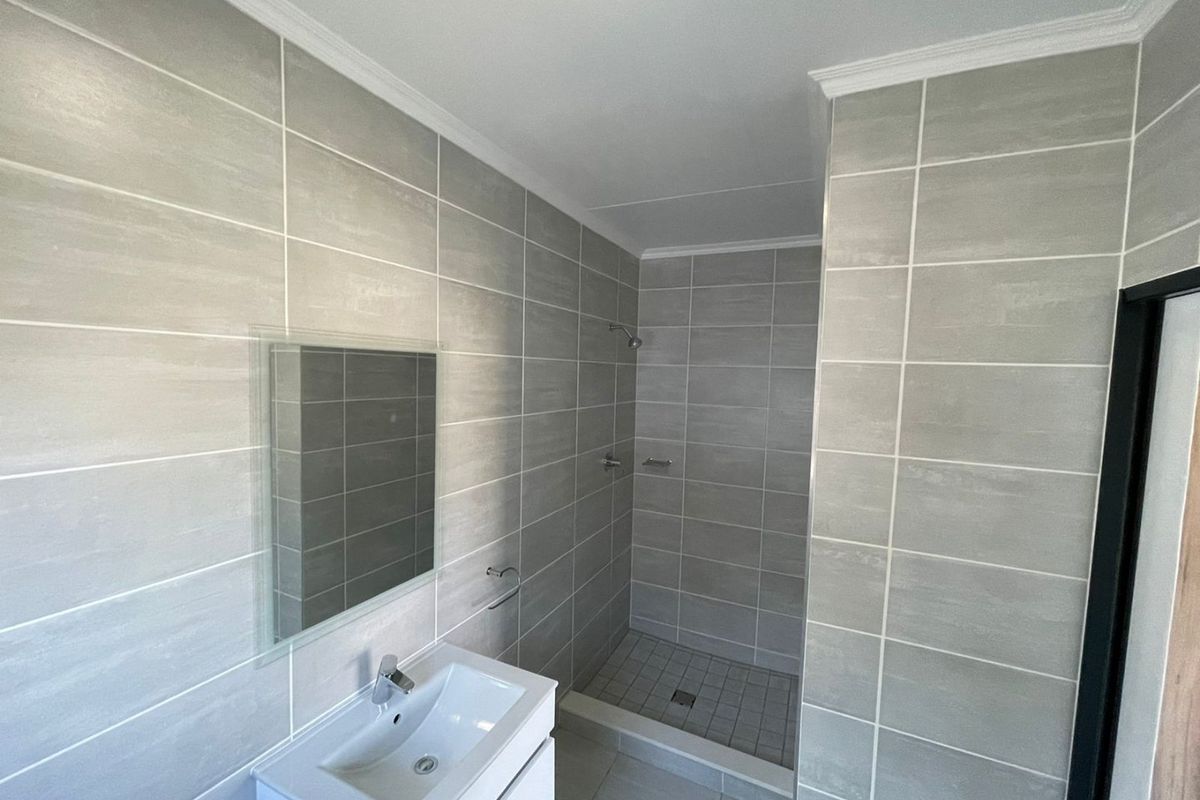 Modern bathroom featuring a walk-in shower, contemporary wall-mounted vanity with basin, and neutral grey wall and floor tiling.