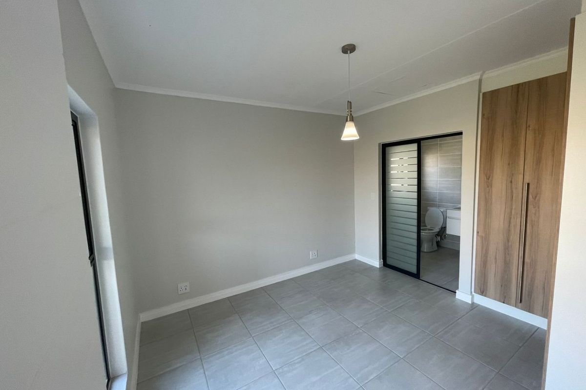 A clean, empty bedroom featuring neutral tiled flooring, built-in wooden cupboards, and direct access to an en-suite bathroom through a sliding door.