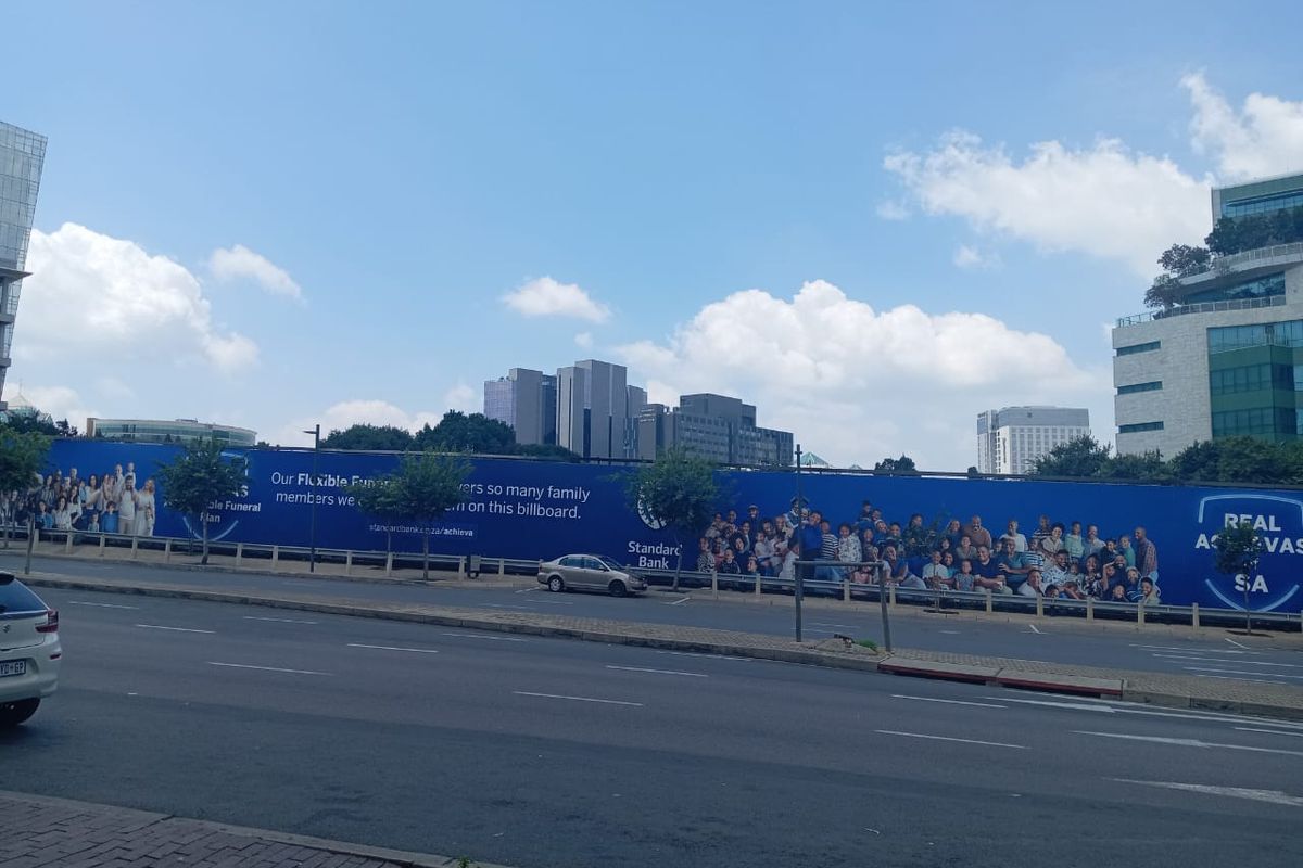 A street-level view of a vacant residential land plot featuring a large advertising billboard along the perimeter.