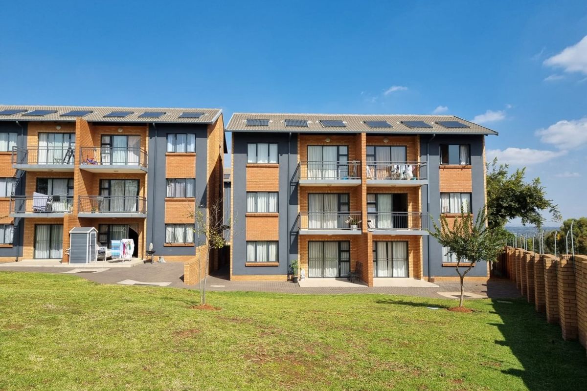 Rear view of a multi-story apartment complex featuring brick facades, private balconies, sliding glass doors, and solar panels, set against a landscaped lawn.