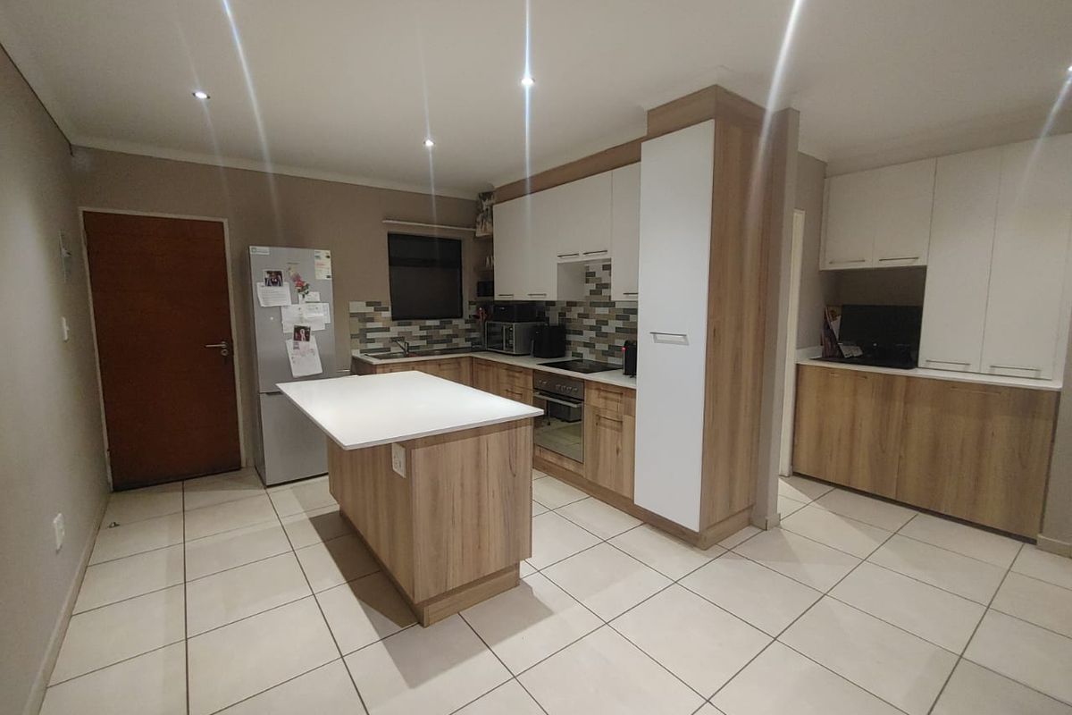 Modern kitchen featuring wood-finish and white cabinetry, a central island with stone countertop, tiled backsplash, and integrated appliances.
