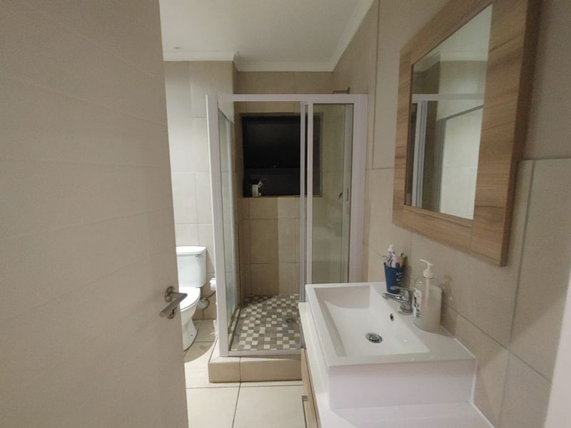 A functional bathroom featuring a shower enclosure, toilet, and a modern vanity basin with a wall-mounted mirror, finished with neutral wall and floor tiles.