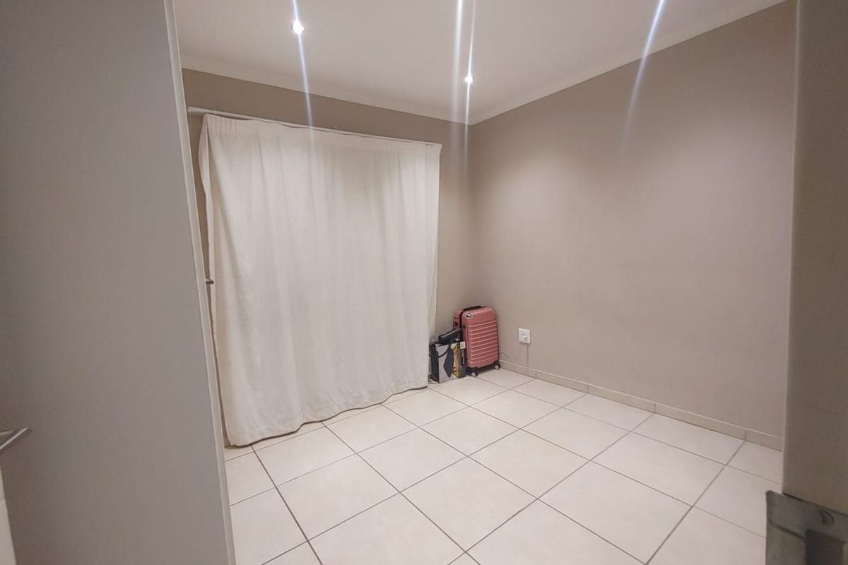 A neutral, empty bedroom featuring tiled flooring and recessed downlighting, providing a blank canvas for personalization.