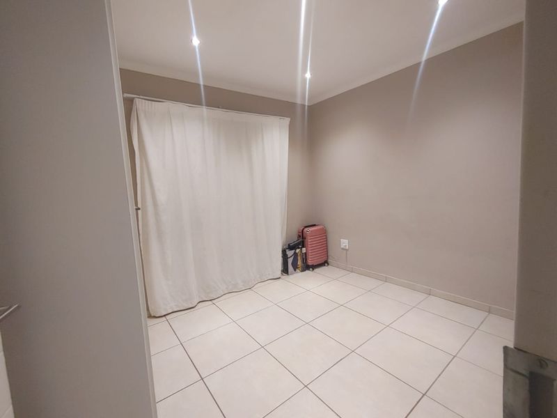 A neutral, empty bedroom featuring tiled flooring and recessed downlighting, providing a blank canvas for personalization.