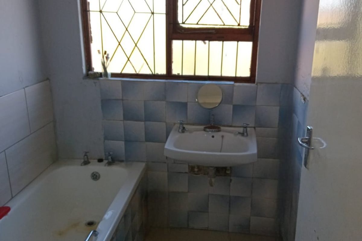 A functional bathroom featuring a bathtub, wall-mounted basin, and tiled finishes, requiring cosmetic updates to modernize the space.