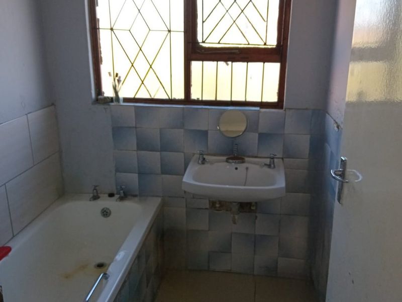 A functional bathroom featuring a bathtub, wall-mounted basin, and tiled finishes, requiring cosmetic updates to modernize the space.