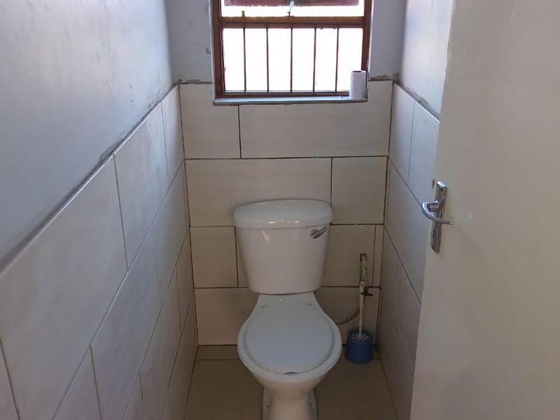 A compact, functional guest toilet featuring tiled walls and flooring, equipped with a window for natural light and security bars.