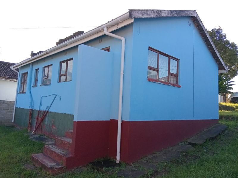 Rear exterior view of the house featuring blue painted walls with a contrasting red plinth, aluminium windows, and concrete steps.