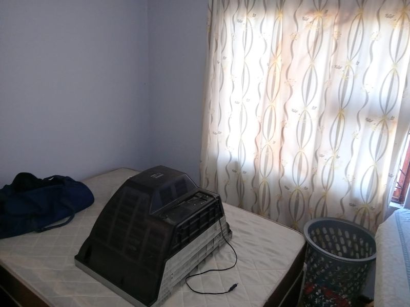 A bedroom space featuring a window with patterned curtains, currently used for storage.