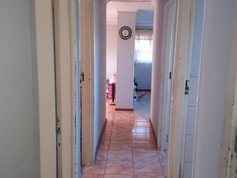 A narrow residential hallway featuring tiled flooring and multiple doorways leading to adjacent rooms, showing signs of wear on the door frames.