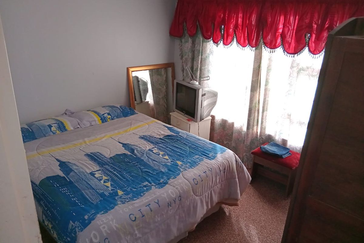 A standard bedroom featuring a window with decorative valance curtains and carpeted flooring.