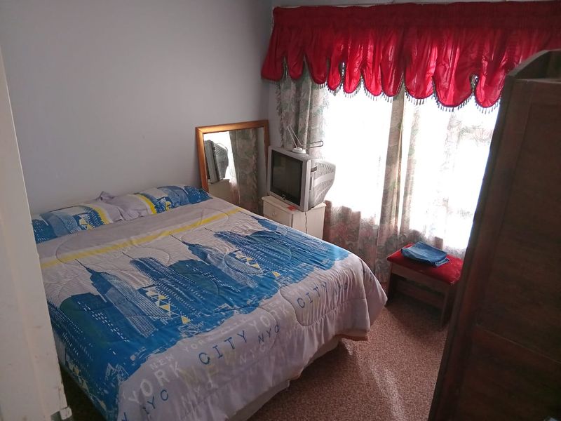 A standard bedroom featuring a window with decorative valance curtains and carpeted flooring.