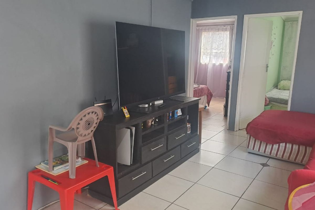 A living room area featuring ceramic floor tiles and access to adjacent bedrooms.