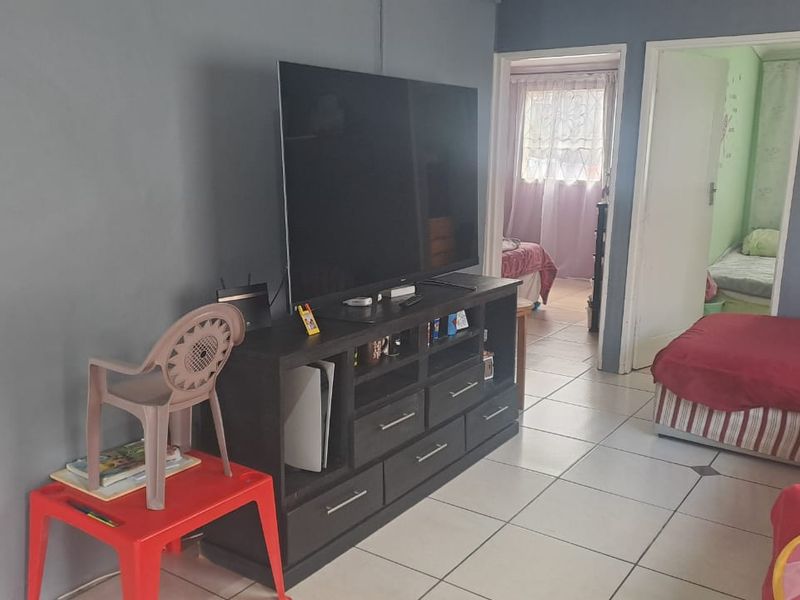 A living room area featuring ceramic floor tiles and access to adjacent bedrooms.