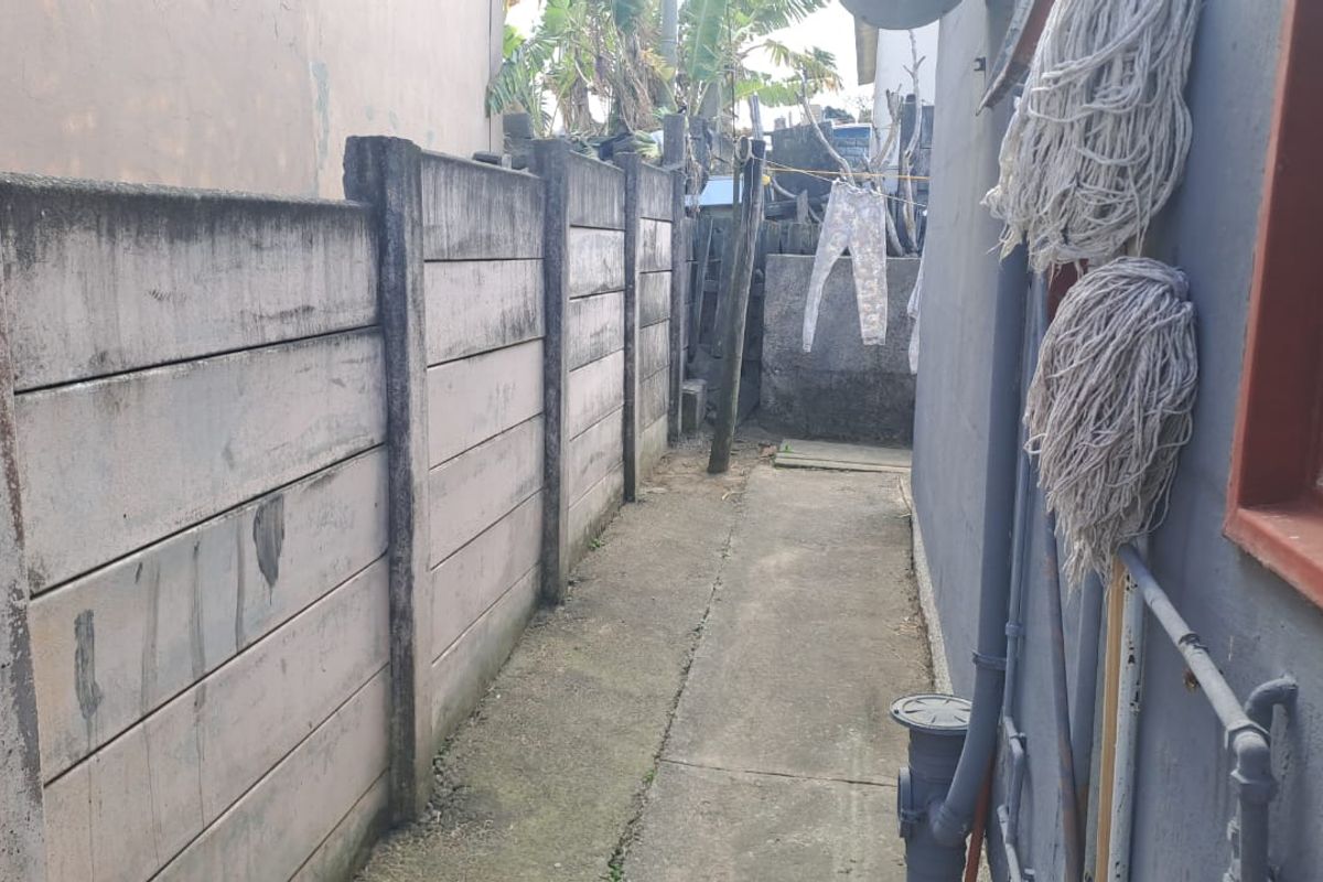A narrow side passage featuring a precast concrete boundary wall and concrete pathway, showing signs of weathering and wear.