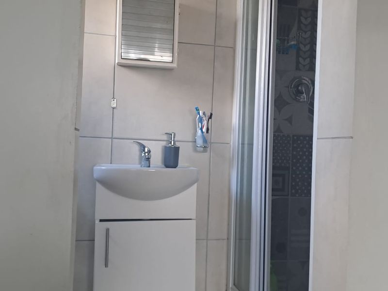 A compact bathroom featuring a modern vanity unit with a basin, a wall-mounted medicine cabinet, and a tiled shower enclosure.