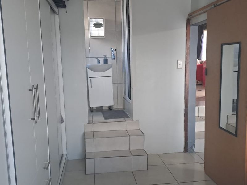 A functional bathroom area featuring a vanity basin, tiled steps, and built-in wardrobe storage, with an adjacent sliding door entrance.