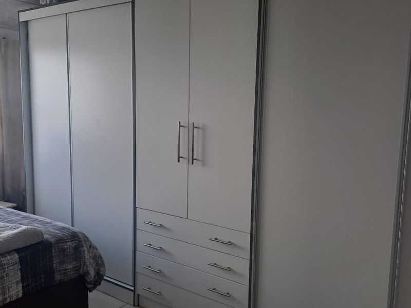 A bedroom featuring modern white built-in cupboards with integrated drawers and sliding door storage.