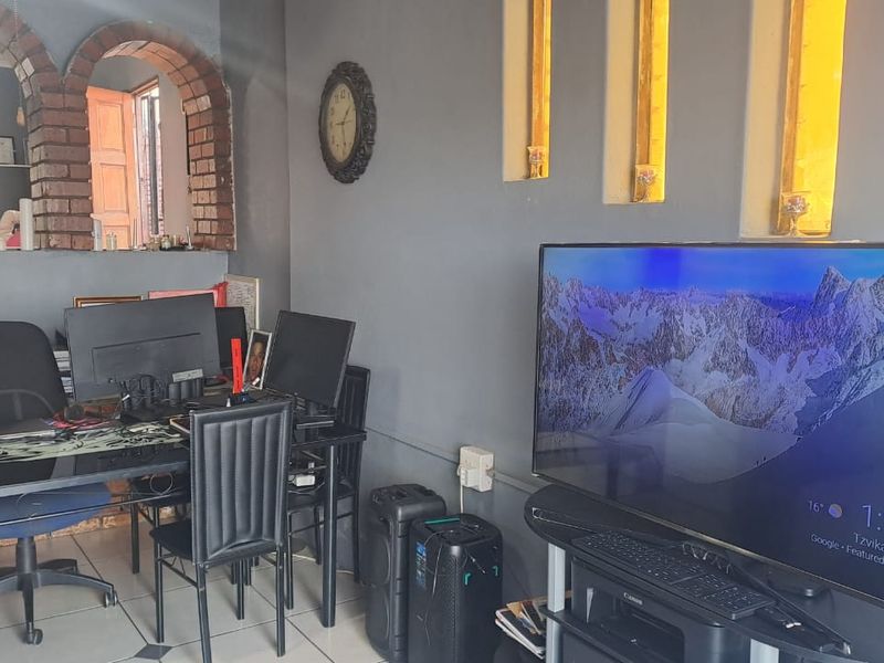 A living area featuring a distinctive brick archway, recessed wall niches, and tiled flooring, currently utilized as a home office space.