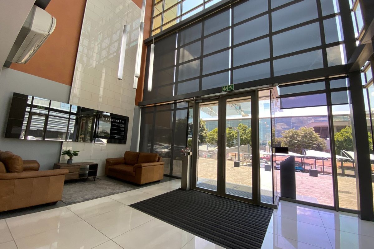 Modern commercial building entrance featuring double-height glass windows, polished tiled flooring, and a contemporary feature wall in a bright, professional lobby space.