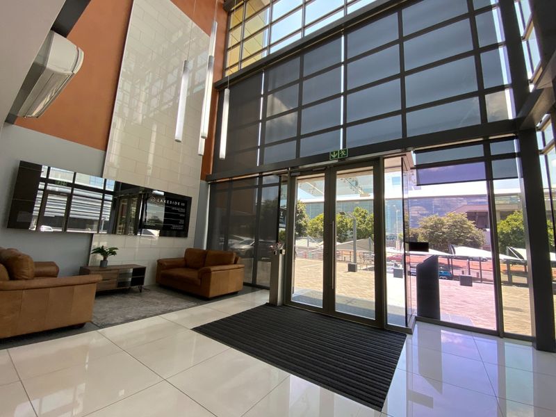 Modern commercial building entrance featuring double-height glass windows, polished tiled flooring, and a contemporary feature wall in a bright, professional lobby space.