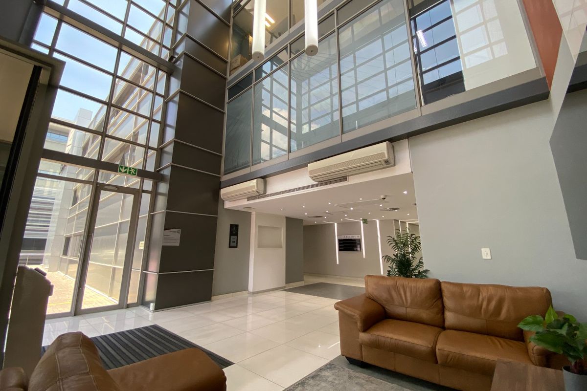 Modern commercial building entrance lobby featuring double-volume glass facade, tiled flooring, and integrated climate control systems.