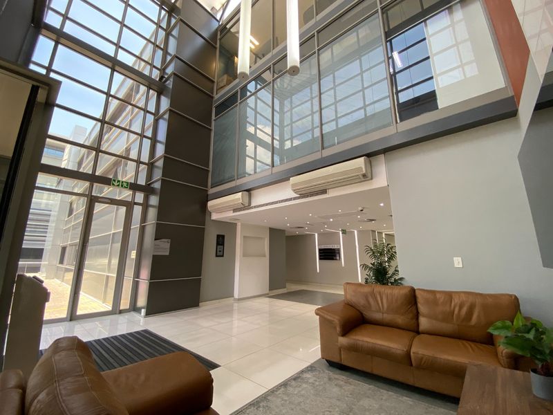 Modern commercial building entrance lobby featuring double-volume glass facade, tiled flooring, and integrated climate control systems.