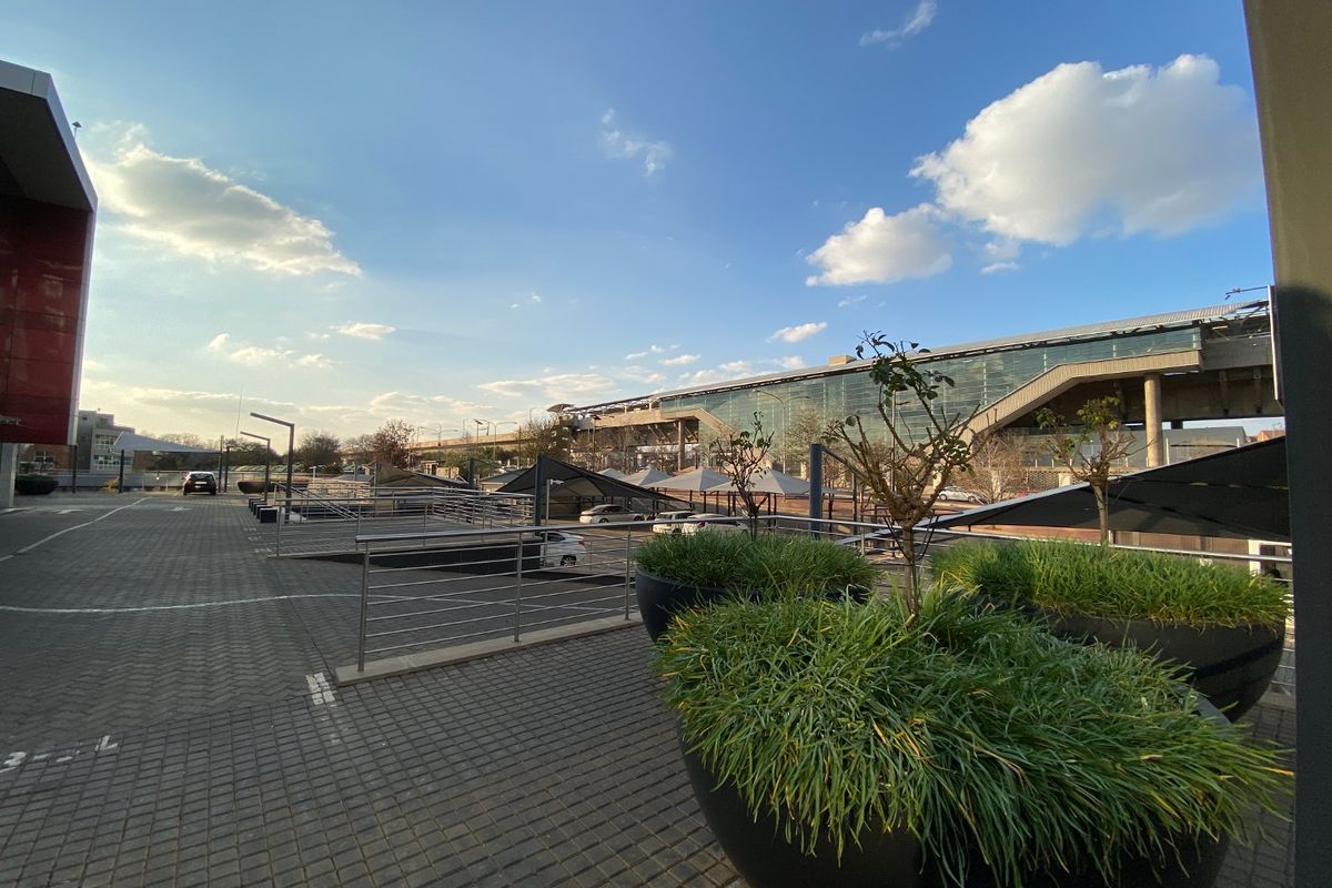 An elevated view of a commercial parking area featuring paved surfaces, metal safety railings, shade structures, and integrated landscaping planters.