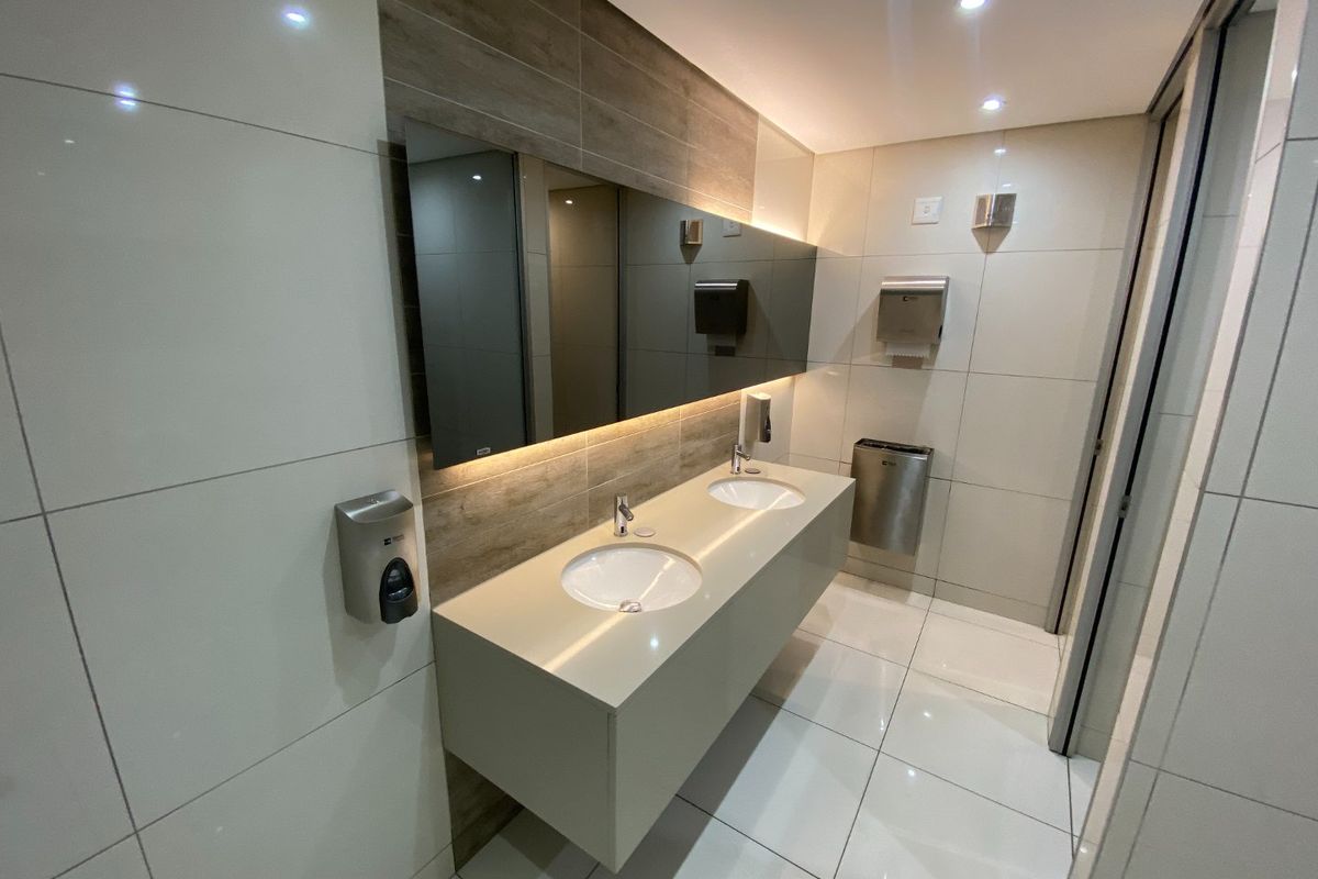 Modern commercial bathroom featuring a sleek double vanity with integrated sinks, large wall-mounted mirror, recessed lighting, and high-quality tiled finishes.