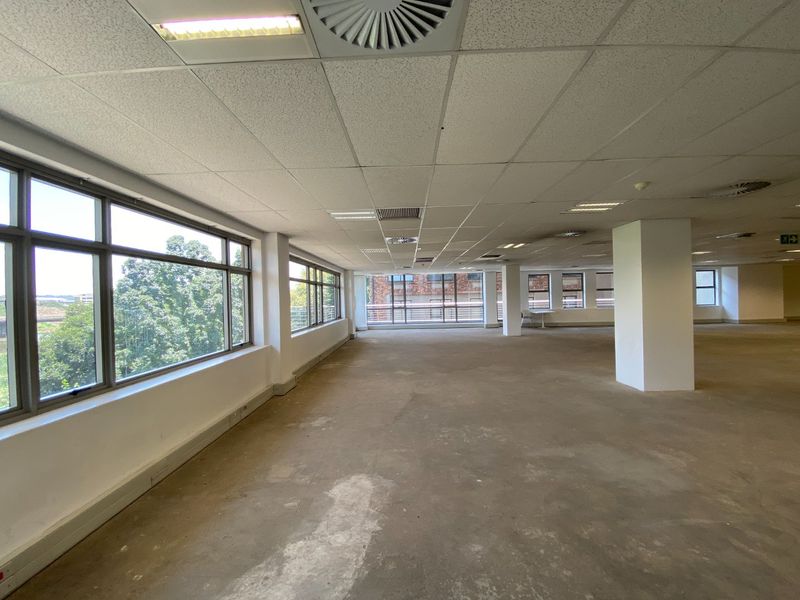 Spacious open-plan commercial office area featuring large windows, suspended ceilings with recessed lighting, and central air conditioning, currently awaiting floor finishing.