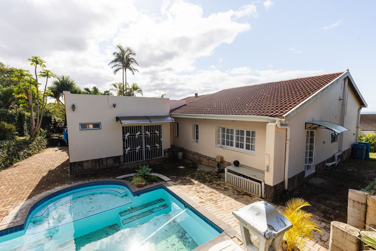 Rear exterior view of the house featuring a swimming pool, paved patio area, and tiled roof structure.