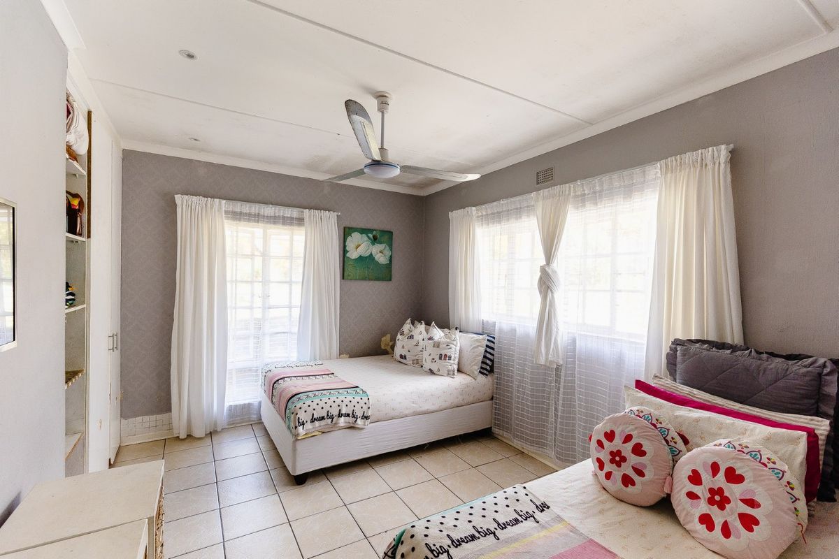 A well-lit bedroom featuring tiled flooring, built-in cupboards, and a ceiling fan, offering a functional and comfortable living space.