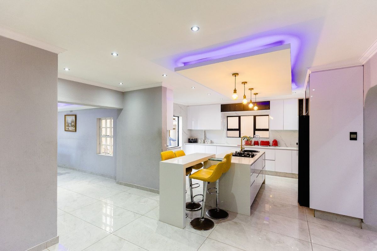 Modern kitchen featuring a central island with breakfast bar, sleek white cabinetry, stone countertops, gas hob, and sophisticated recessed and cove lighting.