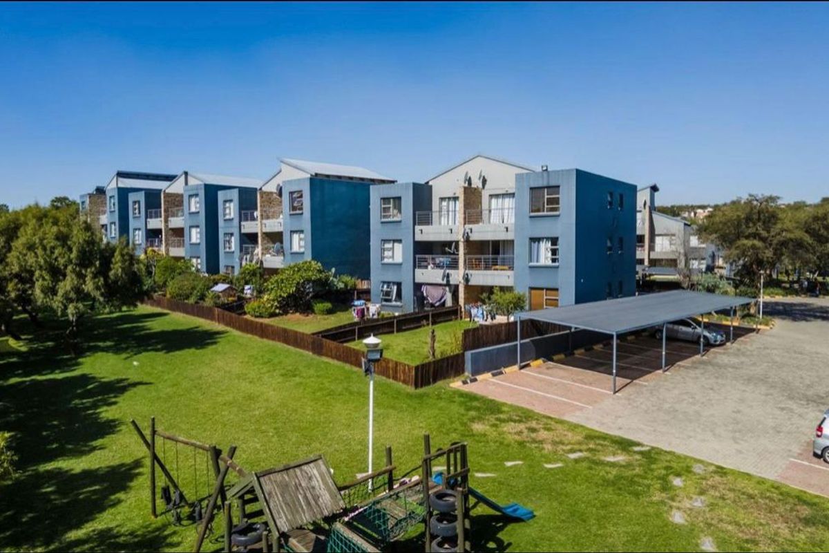 Aerial view of a multi-story apartment complex featuring covered parking, landscaped grounds, and a communal playground area.