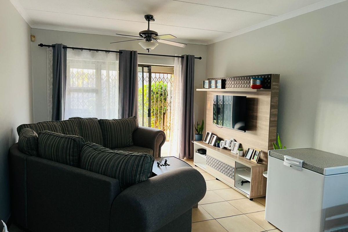 A living room featuring tiled flooring, a ceiling fan, and a sliding glass door with a security gate leading to the exterior.