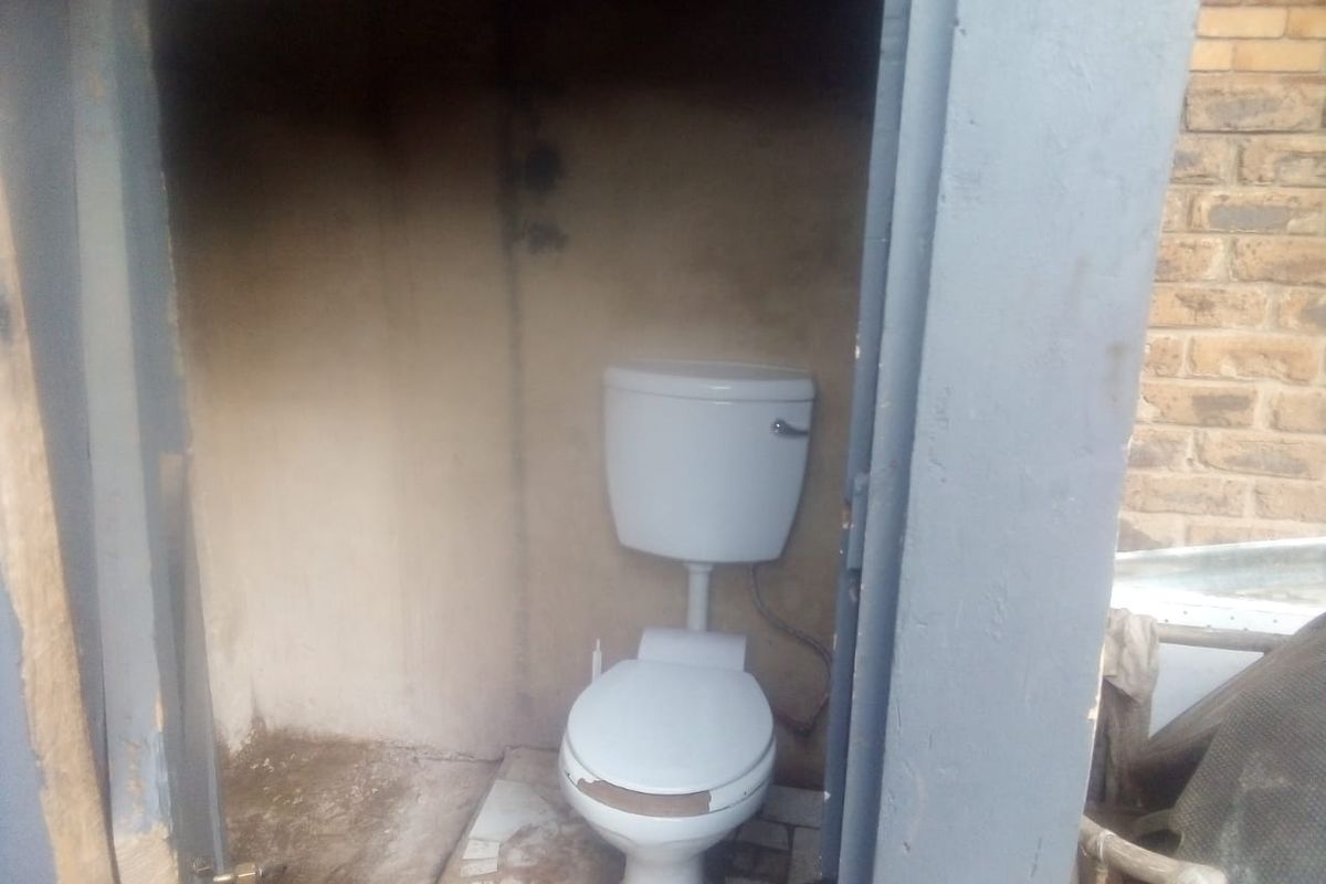 A small, basic outdoor toilet facility requiring significant maintenance and refurbishment of wall and floor finishes.
