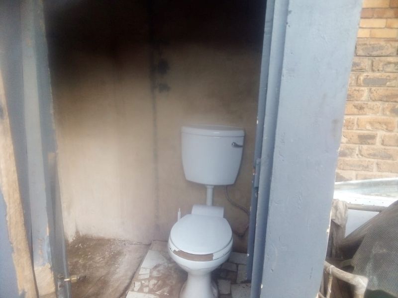 A small, basic outdoor toilet facility requiring significant maintenance and refurbishment of wall and floor finishes.