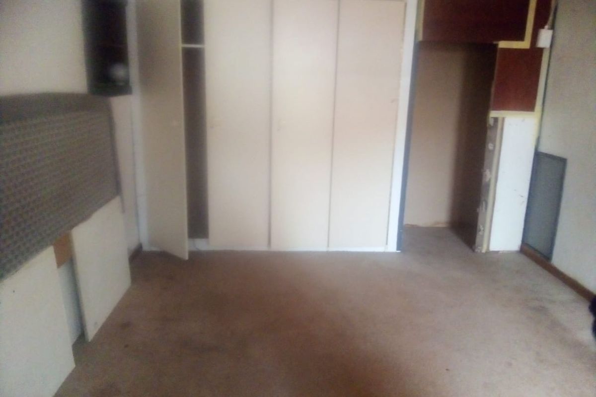 An empty bedroom featuring built-in cupboards and carpeted flooring, currently requiring cosmetic updates and repairs to finishes.