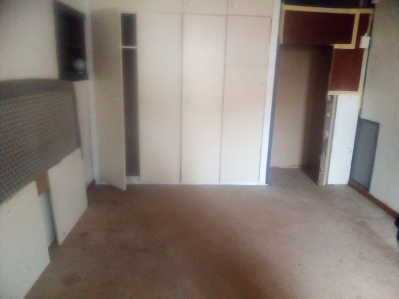 An empty bedroom featuring built-in cupboards and carpeted flooring, currently requiring cosmetic updates and repairs to finishes.