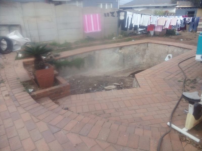 An outdoor pool area featuring brick paving and a concrete boundary wall, currently requiring significant maintenance and restoration of the pool shell.