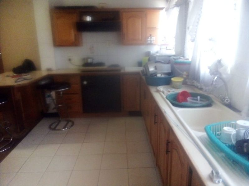 A dated kitchen featuring wooden cabinetry, a built-in oven, extractor fan, and a double basin sink with tiled flooring.