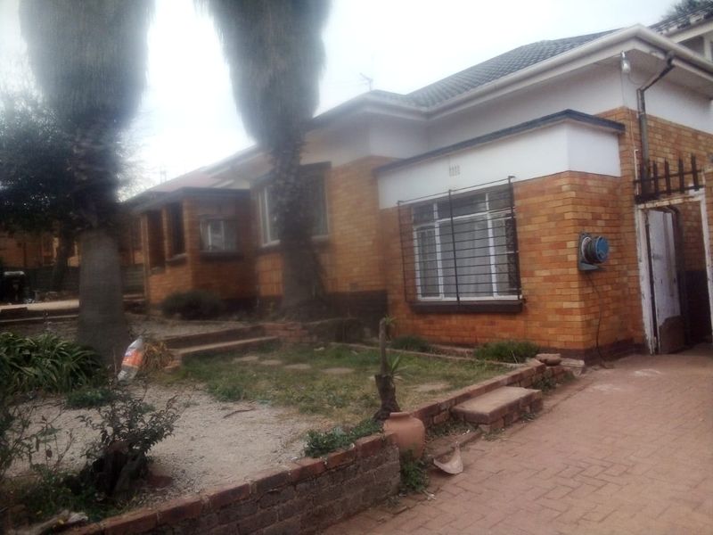 Front exterior view of a single-story brick house featuring a paved driveway, security bars on windows, and a small front garden area.