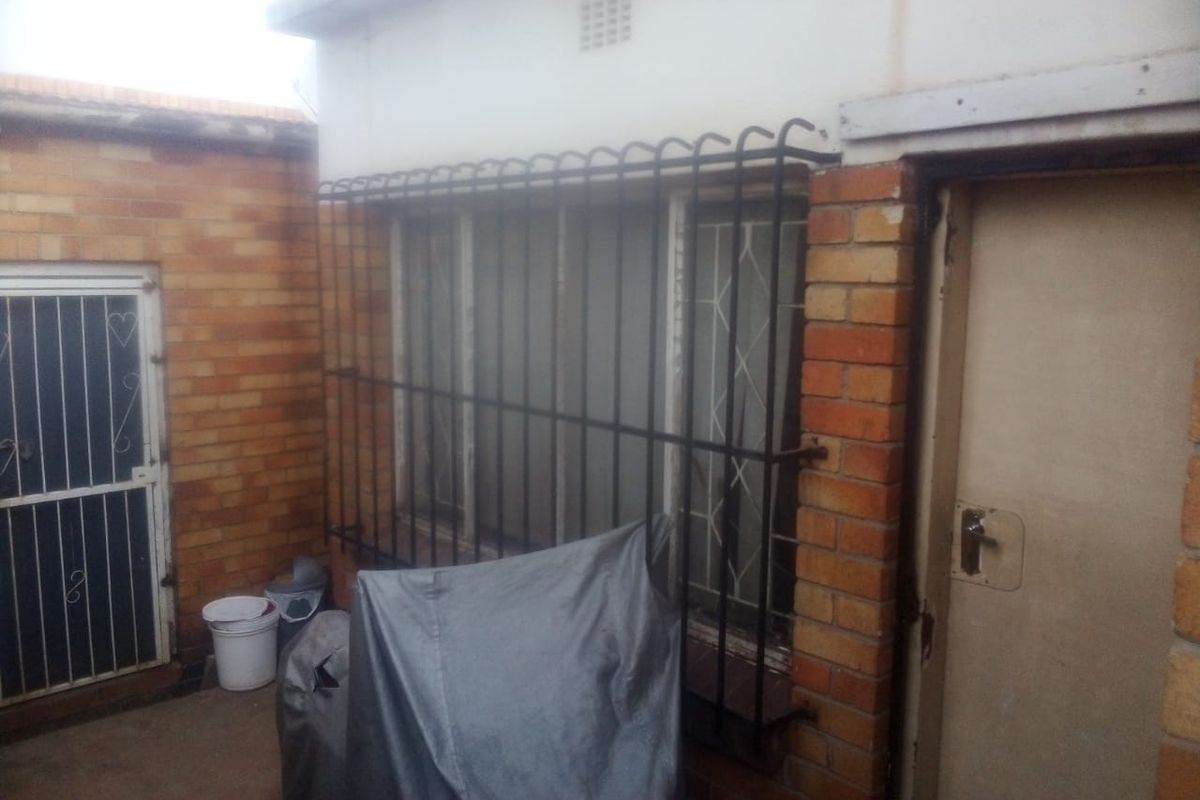 Rear exterior view of the property featuring brick walls, security bars on windows, and a secure entrance door.