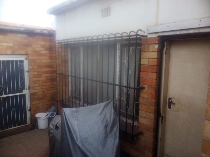 Rear exterior view of the property featuring brick walls, security bars on windows, and a secure entrance door.