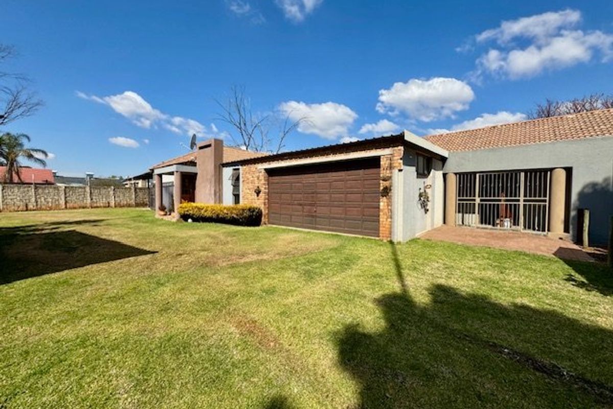 Rear view of the property featuring a double garage, paved patio area, and a spacious garden enclosed by a perimeter wall.