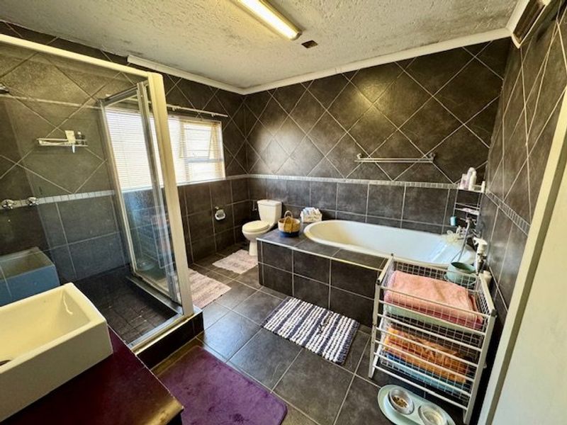 A full bathroom featuring a shower enclosure, built-in bathtub, toilet, and basin with dark tiled walls and flooring.