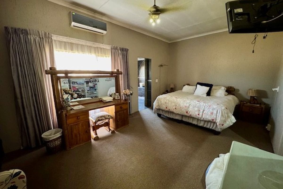 Spacious bedroom featuring carpeted flooring, a ceiling fan, and a wall-mounted split-system air conditioner.
