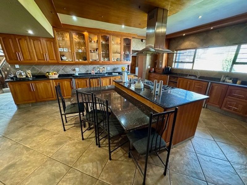 Spacious kitchen featuring extensive wooden cabinetry, granite countertops, a central island with integrated hob, and a stainless steel extractor fan.