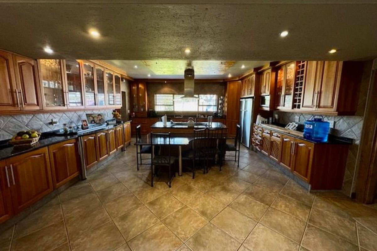 Spacious kitchen featuring extensive wooden cabinetry, granite countertops, a central island, and tiled flooring, offering a functional layout with ample storage and workspace.