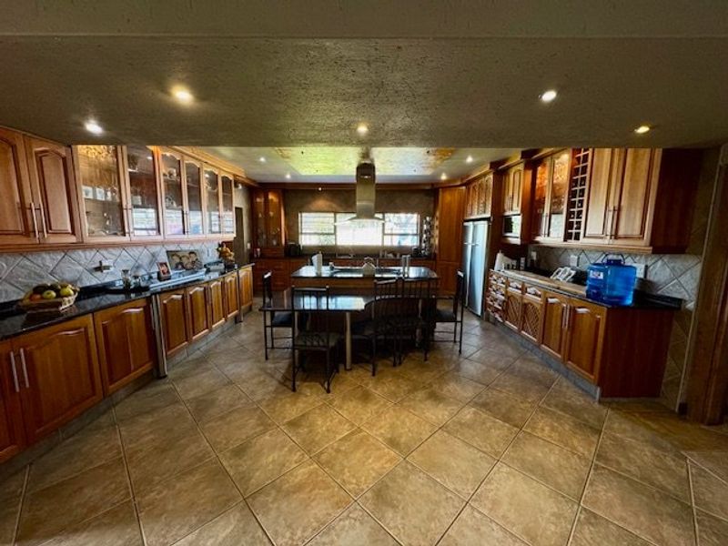 Spacious kitchen featuring extensive wooden cabinetry, granite countertops, a central island, and tiled flooring, offering a functional layout with ample storage and workspace.